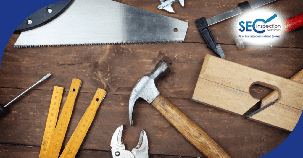 Hand tools including a saw, hammer, and measuring stick arranged on a wooden surface.